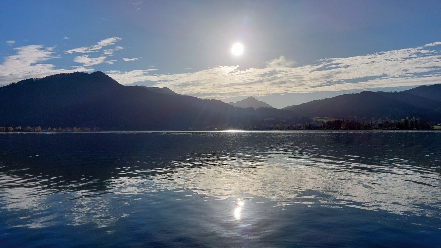 The picture shows a mountain lake in glaring sunlight. A mountain chain is visible in the background.