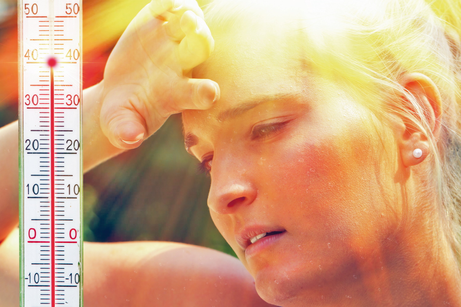 The picture shows a woman’s face with beads of perspiration caused by the summer heat. The woman is holding a hand to her forehead. In the left-hand side of the picture is a thermometer indicating 40°C air temperature.