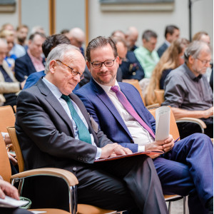 Teilnehmende sitzen auf Stühlen in Reihen und beschäftigen sich mit Schriftgut in ihren Händen.