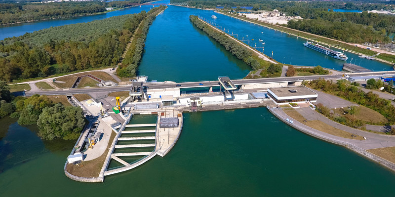 Foto: Das Wasserkraftwerk Iffezheim samt Staustufe am stark ausgebauten und begradigten Rhein. Im Vordergrund ist ein großer Fischpass zu sehen.