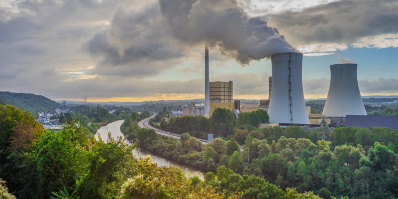 Foto: Zwei Kühltürme eines Wärmekraftwerks im unmittelbaren Umfeld eines Flusses. Aus einem Kühlturm tritt Wasserdampf aus.