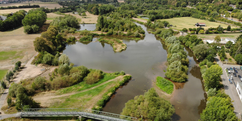 Luftbild der Fulda mit weit ausladenden Nebengewässern. Entlang der Ufer wachsen größtenteils Gehölze. Im Vordergrund ist eine Fußgängerbrücke zu sehen.