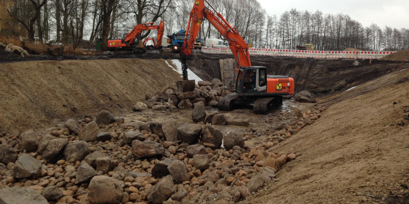 Foto: Die Fischaufstiegsanlage während der Bauarbeiten. Ein Bagger steht im Gewässerbett und setzt große Wasserbausteine ein.