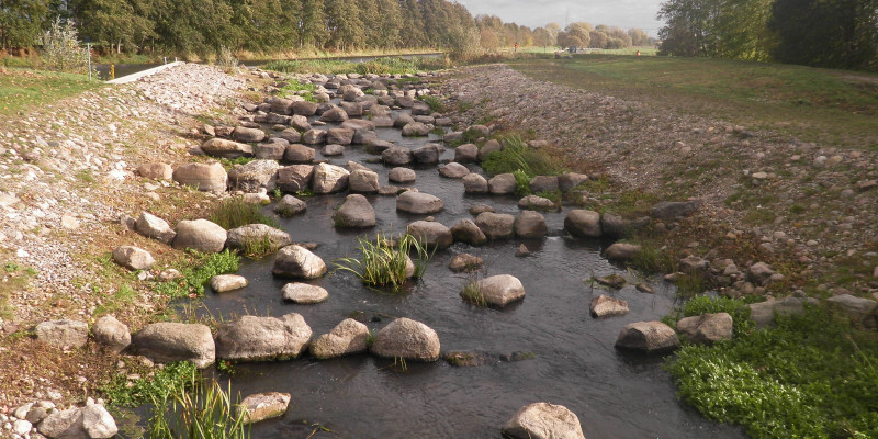 Foto: Die fertiggestellte Fischaufstiegsanlage in Lüssow. Eine langgezogene Gleite mit vielen größeren Steinblöcke im Gewässer ersetzt das alte Streichwehr.