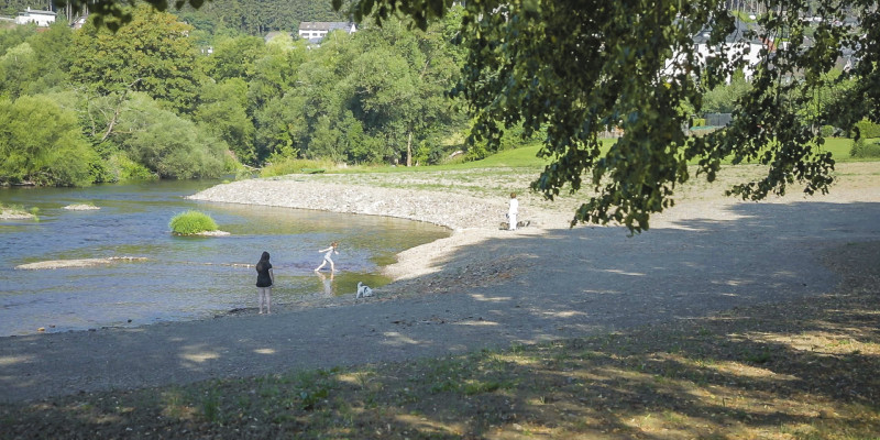 Foto: Erholungssuchende Menschen an der renaturierten Ruhr in Oeventrop. Im Gewässer befinden sich kleine Kiesbänke. Im Hintergrund wächst üppige Vegetation entlang der Ufer.