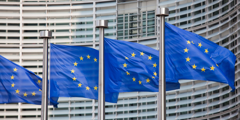Zu sehen sind EU Fahnen und im Hintergrund die Fassade des Gebäudes der EU Kommission