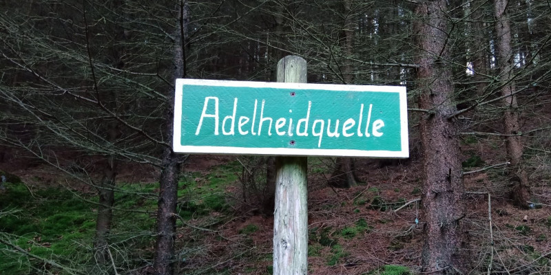 Auf dem Bild ist ein Schild mit der Aufschrift Adelheidquelle dargestellt