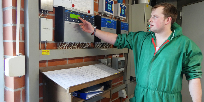 Landwirt in Schutzkleidung vor Anzeigetafel eines digitalen Monitoringsystems.