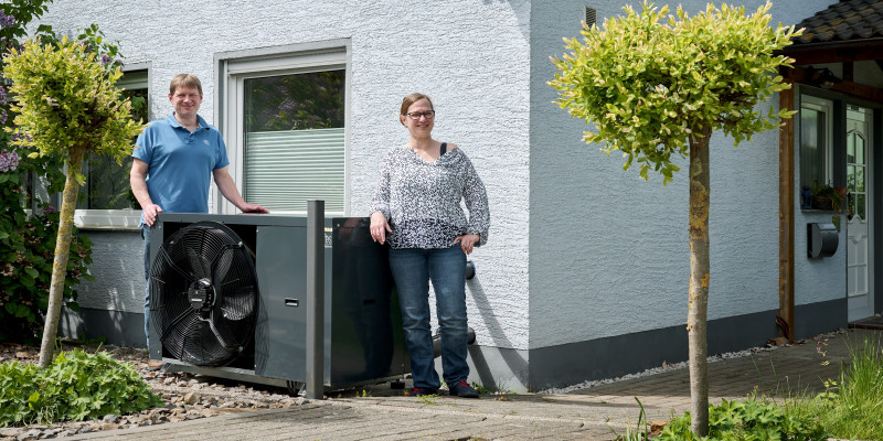 Ein Ehepaar steht vor seinem Haus neben einer Wärmepumpe