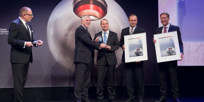 on a stage with a big poster "deutscher nachhaltigkeitspreis 2013" Jochen Flasbarth hands the trophy to a smiling man dressed in a black suit