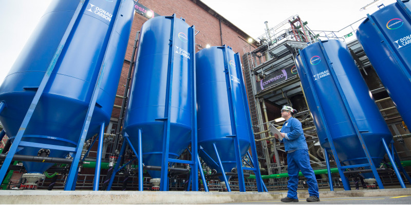 Mann in Arbeitskleidung vor 5 riesigen blauen Tanks vor einer Werkhalle