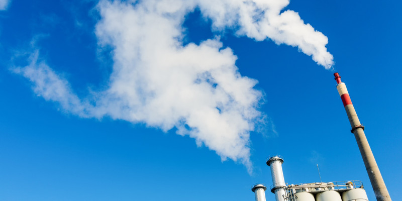 rauchende Schornsteine einer Industrieanlage vor blauem Himmel
