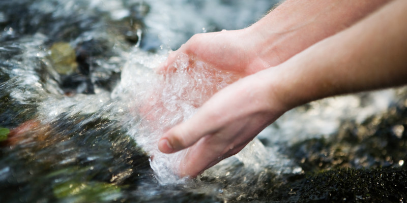 ein Mensch hält seine Hände in einen Bach mit klarem Wasser