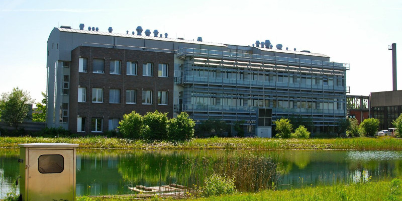 Modern three-storey, elongated office building, with river or canal with grassy banks at the front