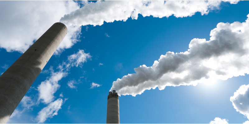 aus Industrieschornsteinen steigt Rauch in blauen Himmel auf