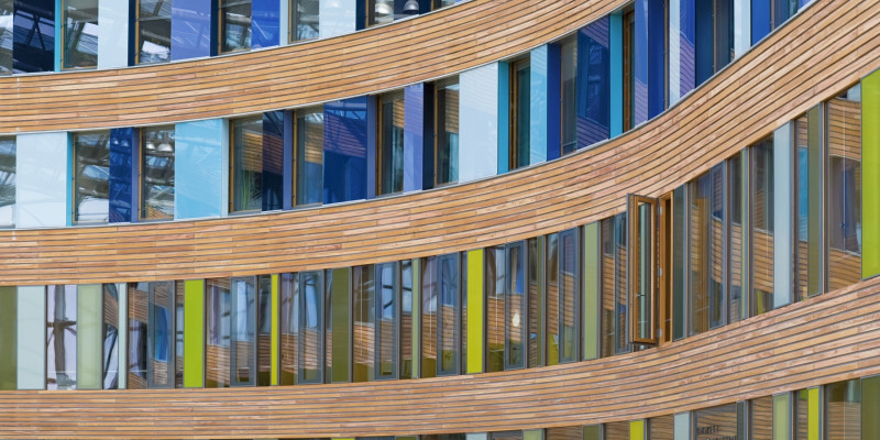 Façade with windows, wood planking and coloured glass slabs in shades of blue and green