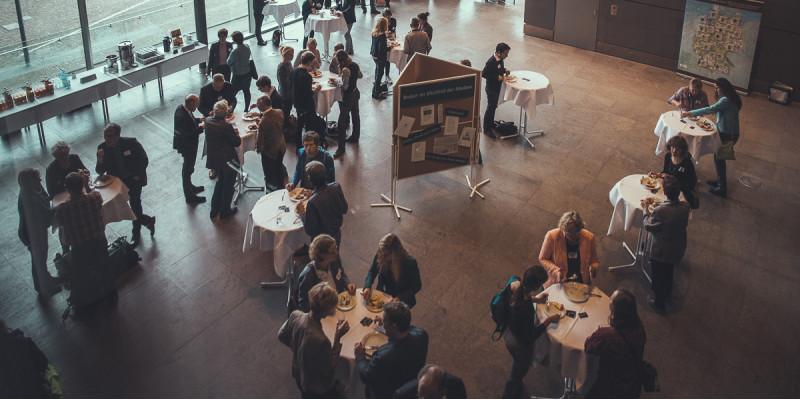 Aufnahme von oben auf die Teilnehmer der Konferenz, die in Grüppchen an Stehtischen stehen