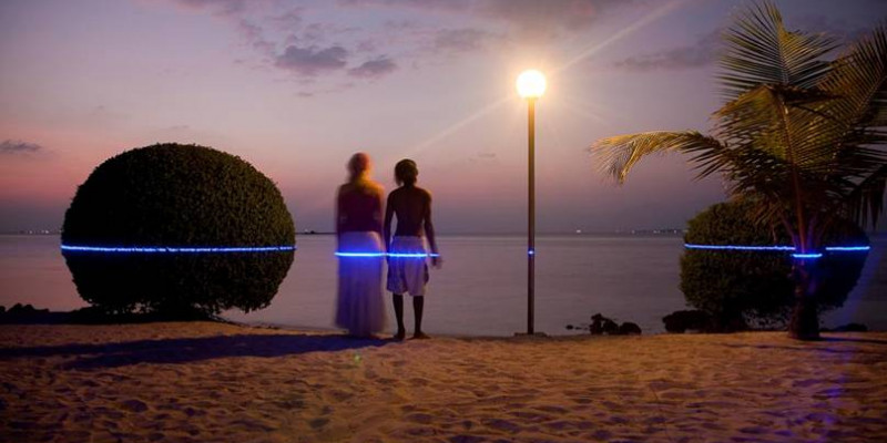 Ein Pärchen steht am Strand blickt in den Sonnenuntergang über dem Meer. In Hüfthöhe zeigt ein blauer Laser, wie hoch Ihnen das Wasser stehen könnte. 