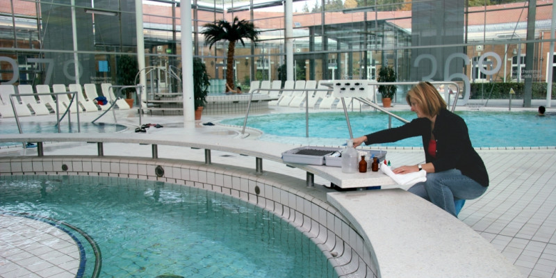 Eine Frau entnimmt in einem öffentlichen Hallenbad eine Wasserprobe aus einem Schwimmbecken.