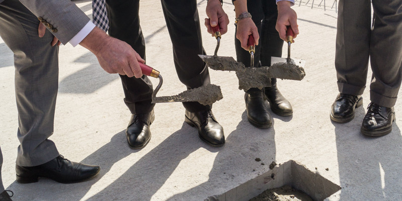 UBA-Präsidentin Maria Krautzberger und Umweltstaatssekretär Jochen Flasbarth stehen auf dem Fundament der Baustelle und spachteln das letzte Loch mit der Zeitkapsel zu.