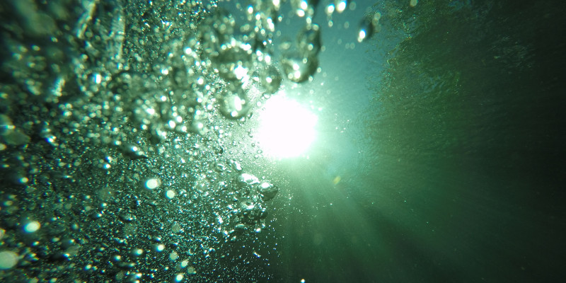 Luftblasen erheben sich beim Tauchen Richtung Wasseroberfläche und Sonne