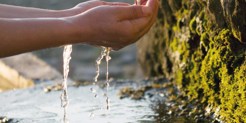 Das Bild zeigt zwei Hände, die Wasser aus einer Quelle auffangen.