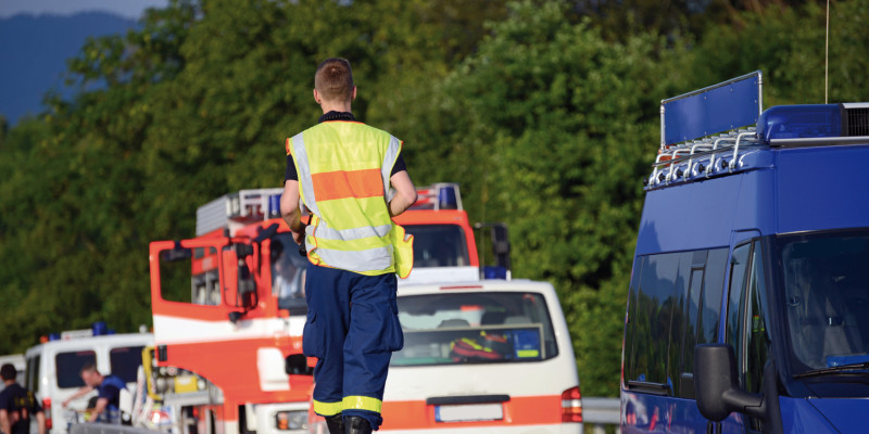 Das Bild zeigt drei Einsatzfahrzeuge der Feuerwehr und des Technischen Hilfswerks, die auf einer Überlandstraße stehen, darunter ein Löschgruppenfahrzeug. Ein Mann mit Warnweste und Einsatzhose des THW läuft auf der Mittelleitplanke.