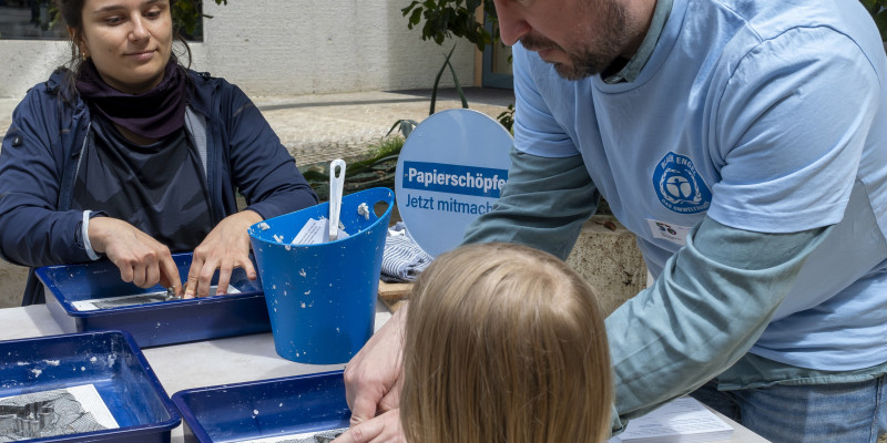 Gäste und Standbetreuer mit Altpapier, Wasser und Formen mit dem Umweltzeichen Blauer Engel, um daraus einen Engel zu schöpfen. 