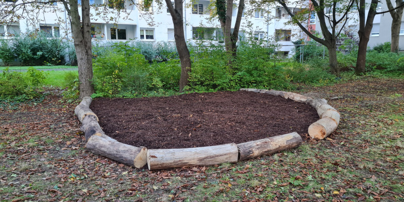 Zu sehen ist eine halbmondförmige Sitzecke, die mit Mulch ausgefüllt und von Baumstämmen umrandet ist.