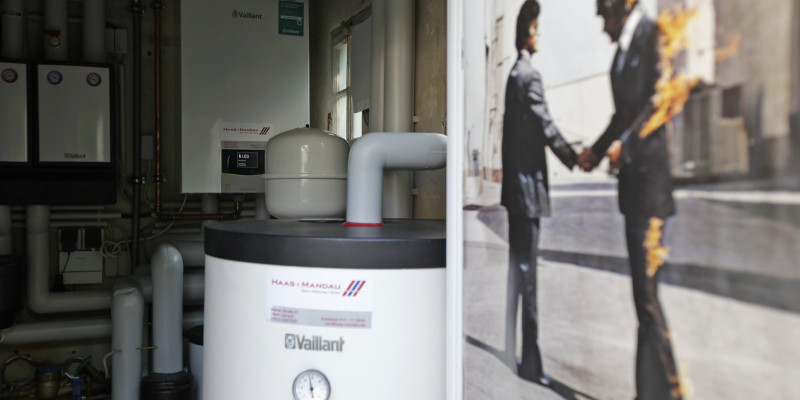 Blick in den Technikraum mit der wandhängenden Gas-Brennwertanlage im Hintergrund, davor der Pufferspeicher und ein Filmplakat