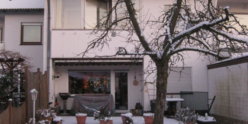 Ein zweistöckiges Reihenhaus mit Terrasse und Balkon in verschneitem Garten.