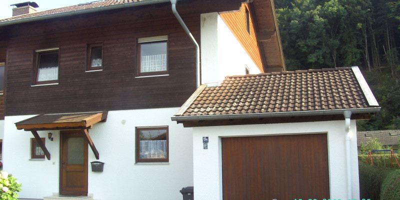 Eine zweistöckige Doppelhaushälfte mit holzverkleidetem Obergeschoss und angebauter Garage