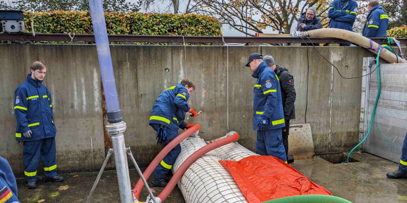 Personen montieren das mobile Hochwasserschutz System 2 teilweise mit gelb/grünen Röhren. Sie tragen gelb/grüne Arbeitskleidung.