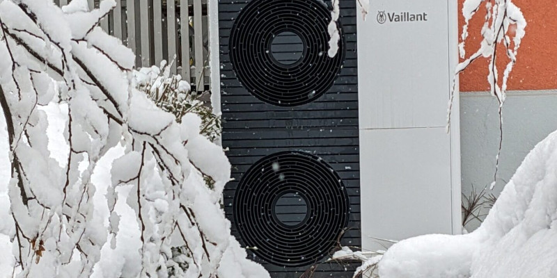 Außengerät einer Wärmepumpe vor einem Gebäude. Im Gerät zwei Lüfter, auf dem Gerät und in der Umgebung liegt 10 cm Schnee.