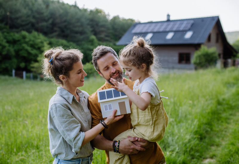 Familie im Vordergrund blickend auf ein Miniatur-Hausmodell 