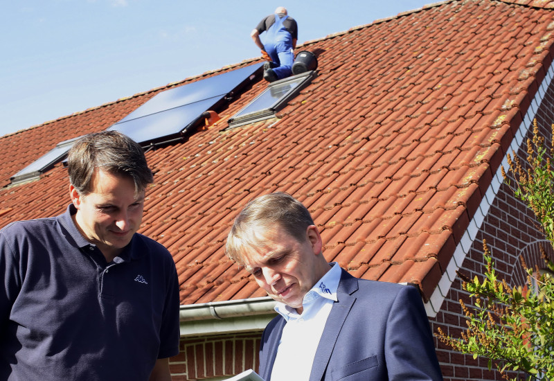 Vorort-Energieberatung vor einem Einfamilienhaus, auf dem Dach ist eine Solarthermieanlage zu sehen