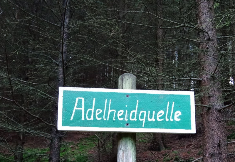 Auf dem Bild ist ein Schild mit der Aufschrift Adelheidquelle dargestellt