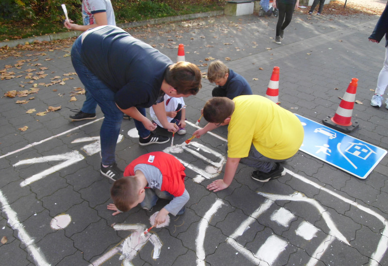 Eltern und Kinder malen das Straßenschild "verkehrsberuhigter Bereich" auf den Asphalt