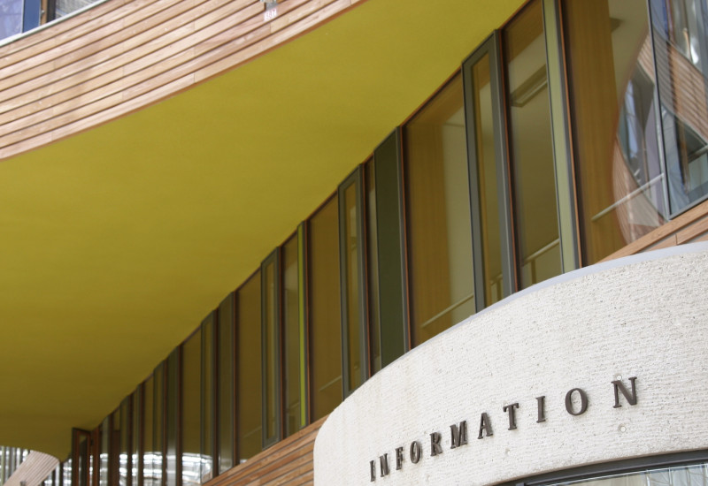 Foto im Innenhof: Moderne Innenfassade mit Glasscheiben, farbigen Flächen und Holz sowie Pförtnerloge mit der Aufschrift "Information"