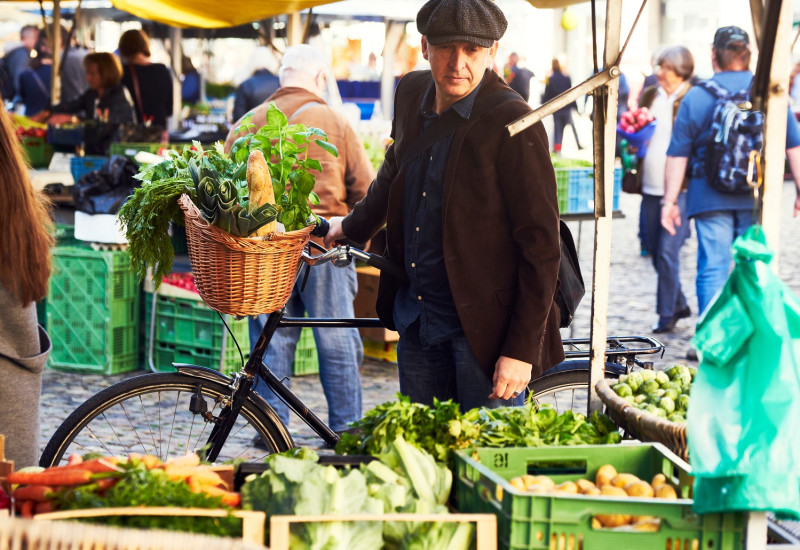 ein Mann kauft mit dem Fahrrad Gemüse auf einem Wochenmarkt ein