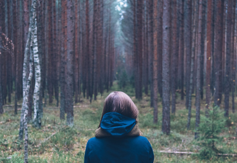 Frau steht mit Rücken zugewandt im Wald.