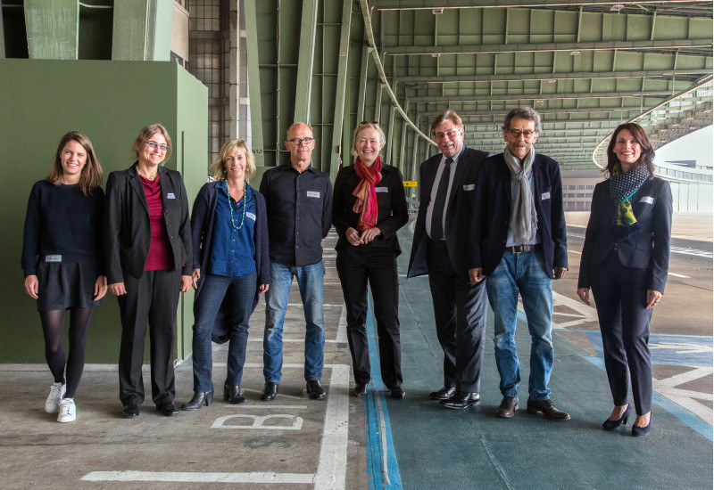 Zu sehen sind die acht Personen der Jury auf dem Rollfeld des ehemaligen Berliner Flughafens in Tempelhof.