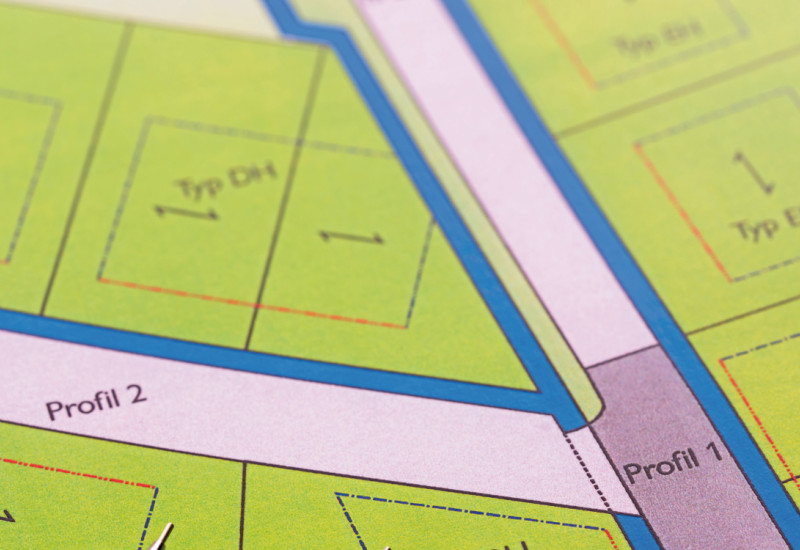 The picture shows an excerpt from a development plan for a residential area with semi-detached and terraced housing. There are two mechanical pencils lying on the plan.