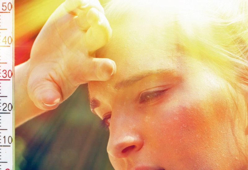 Das Bild zeigt das Gesicht einer Frau mit Schweißperlen in der Sommerhitze. Die Frau hält die Hand an die Stirn. Links im Bild ist ein Thermometer abgebildet, das 40 °C Lufttemperatur anzeigt.