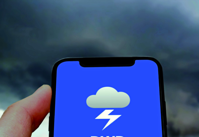 Das Bild zeigt eine Hand, die ein Smartphone hält. Der Bildschirm des Smartphones ist blau und zeigt das Logo der WarnWetter-App des DWD. Im Hintergrund des BIldes sind die schwarzen Wolken eines Gewitterhimmels zu erkennen.