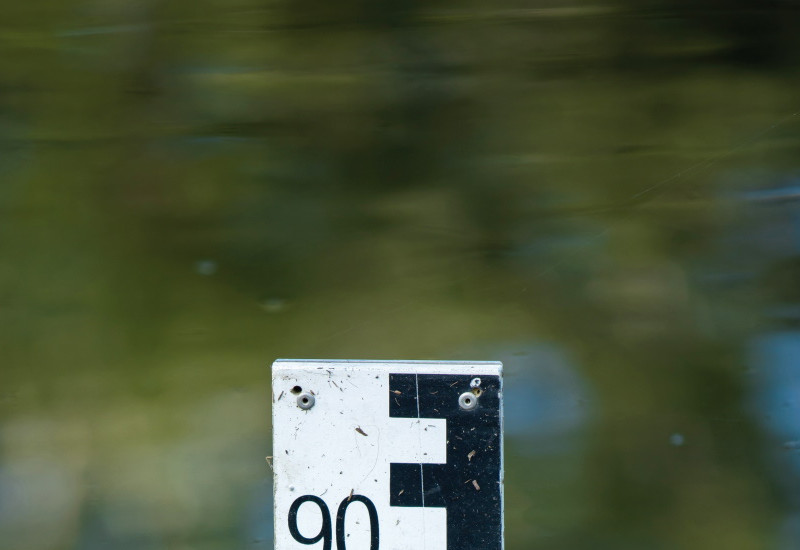 Das Bild zeigt die Spitze einer Pegelmesslatte in einem ruhigen Gewässer.