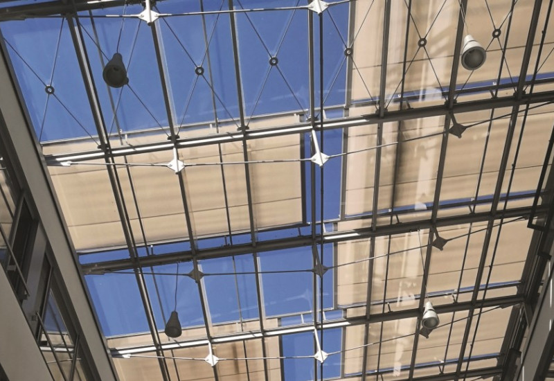 The picture shows the view to the glass roof of an inner courtyard of a modern building, which is partially shaded by textile panels.