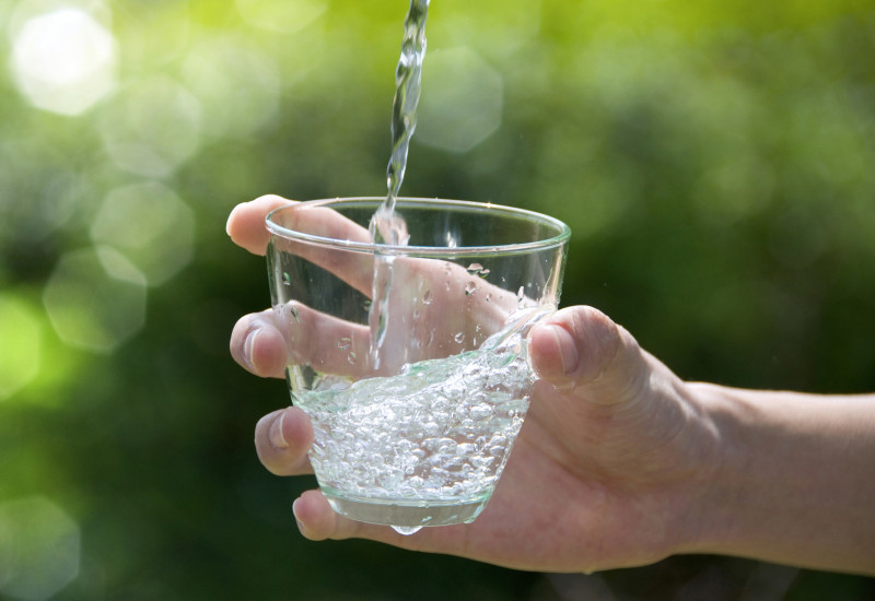 Zu sehen ist eine Hand, die ein Glas hält, in das Wasser gegossen wird. 