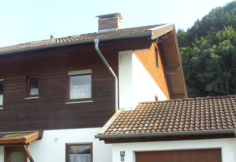 Eine zweistöckige Doppelhaushälfte mit holzverkleidetem Obergeschoss und angebauter Garage