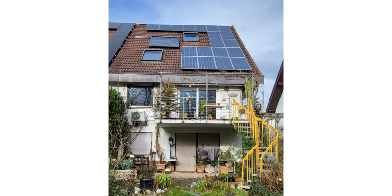 Ein zweistöckiges Haus mit Photovoltaik und Solarthermie auf dem Dach. Im Vordergrund der Garten.